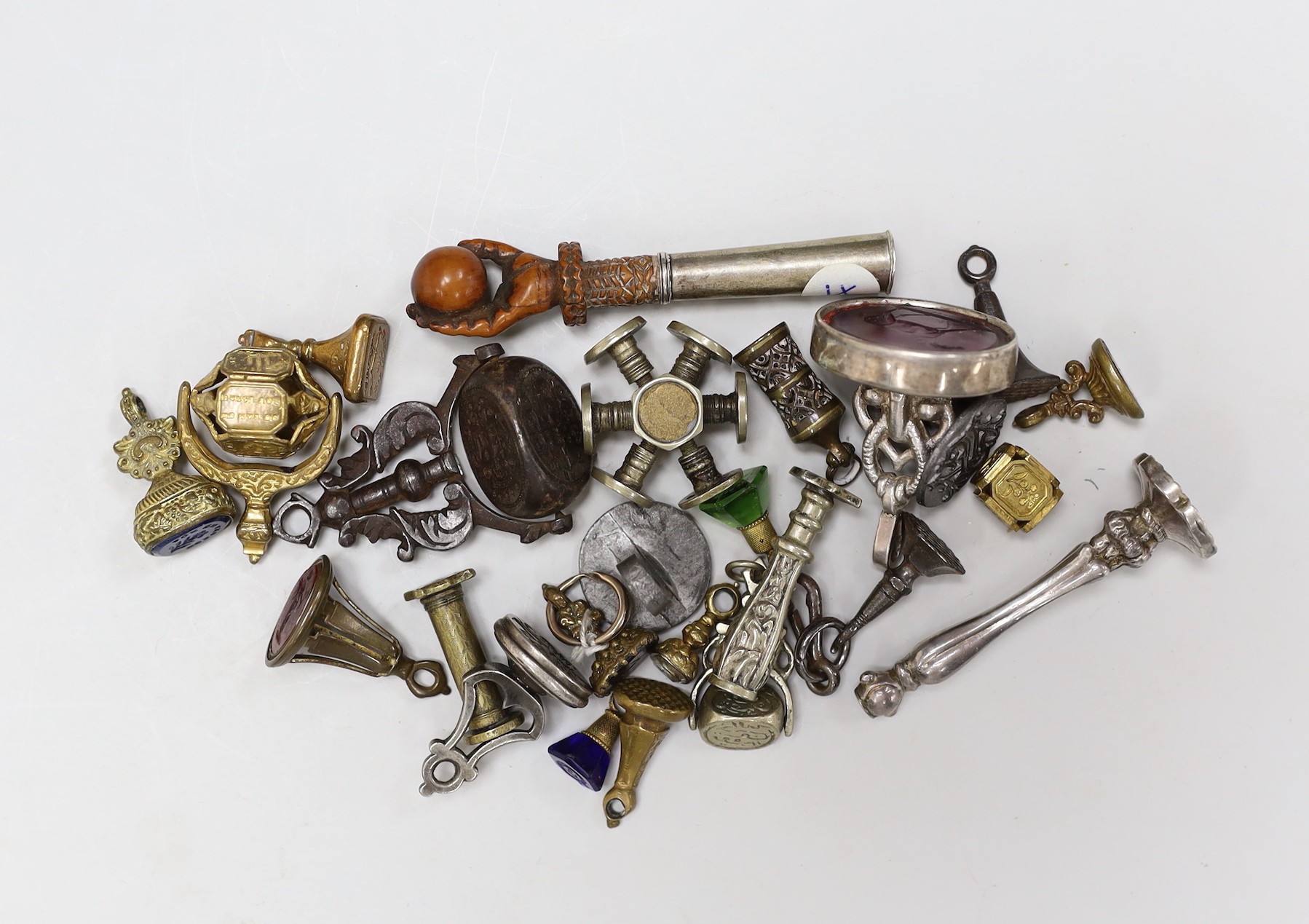 A group of twenty-five steel, gilt metal or nickel fob or desk seals, mostly 19th-century, including a steel swivel seal, a seal with boxwood finial modelled as a hand holding a ball and a nickel multi seal